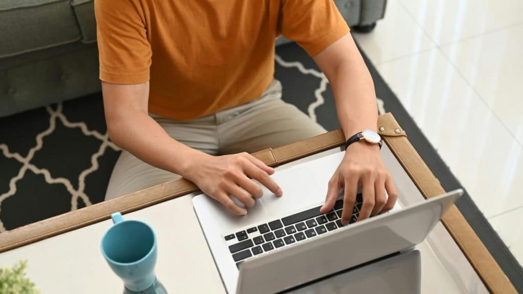 A person typing on a laptop at a coffee table beside a blue mug.