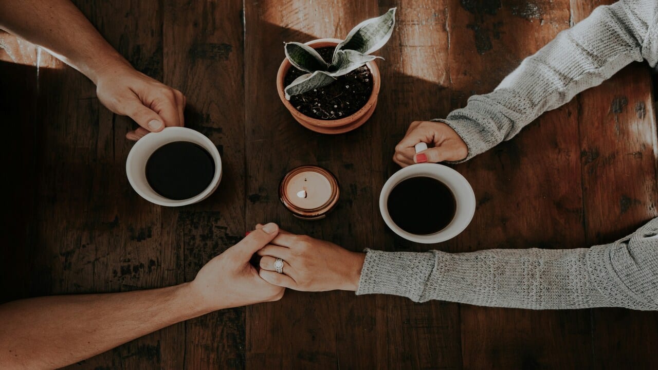 A couple holding hands while having coffee.