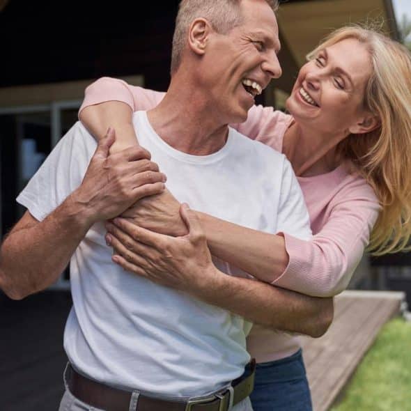A happy middle-aged woman hugging a laughing man outdoors.