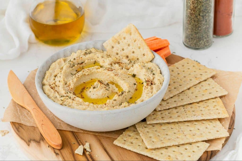 A picture of hummus, crackers and a sliced carrots.