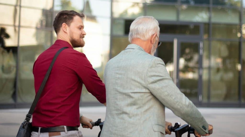 A young man guiding an older man on a scooter.