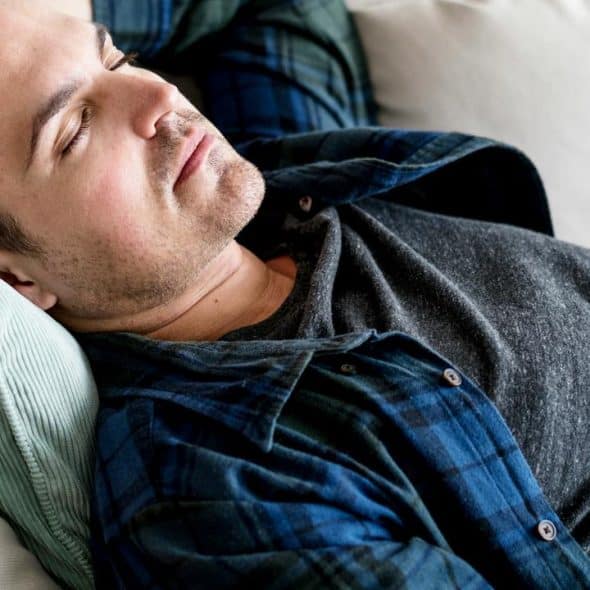 A man reclining on a sofa with a pillow behind his head.