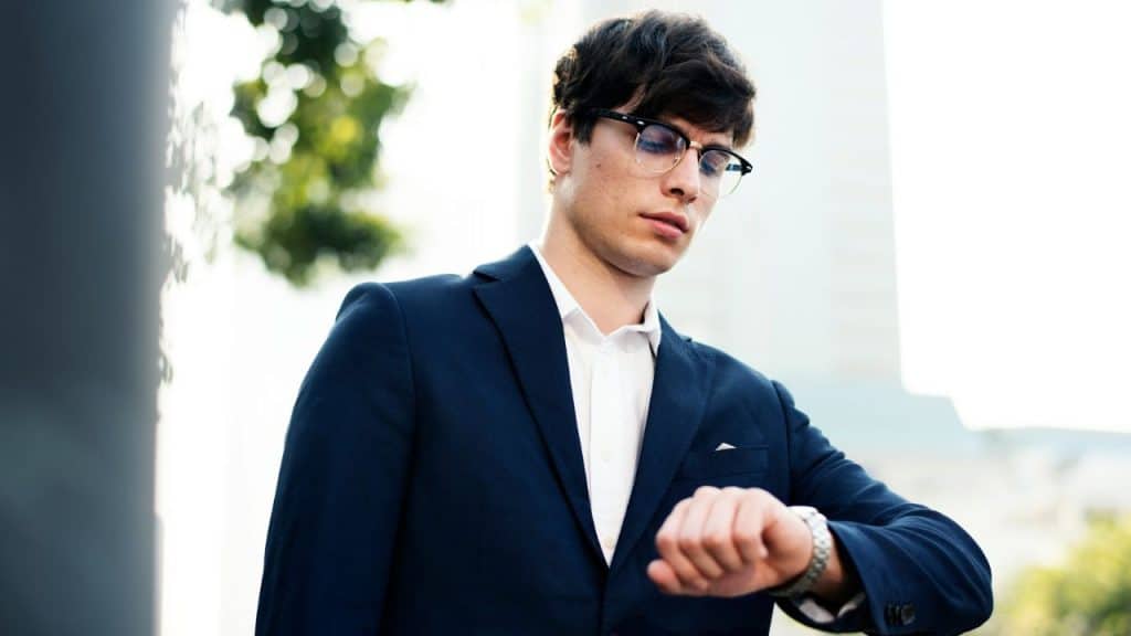 A stylish man in a suit and glasses looks at his watch.