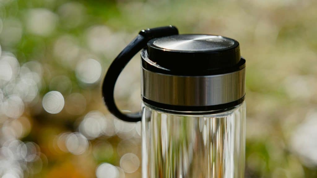 A stainless steel travel mug with a black lid and handle against a blurred background.