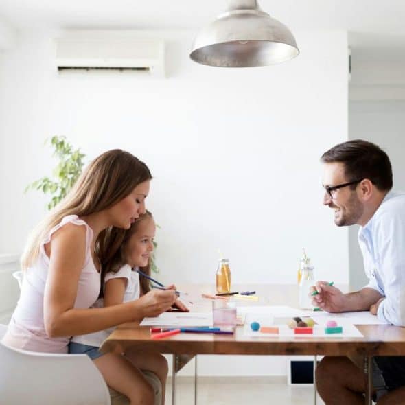 A family of three drawing together at a table.