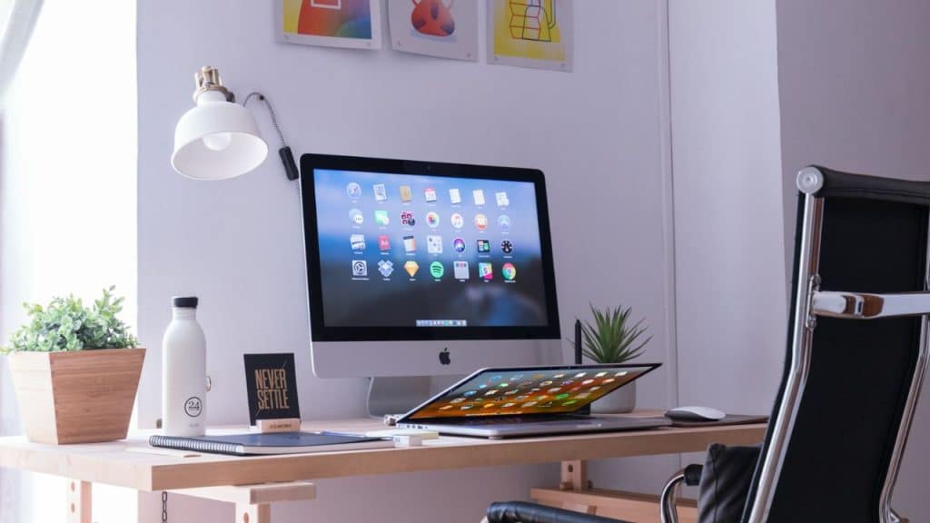 A bright, modern workspace with a desktop computer, laptop, lamp, and plants.