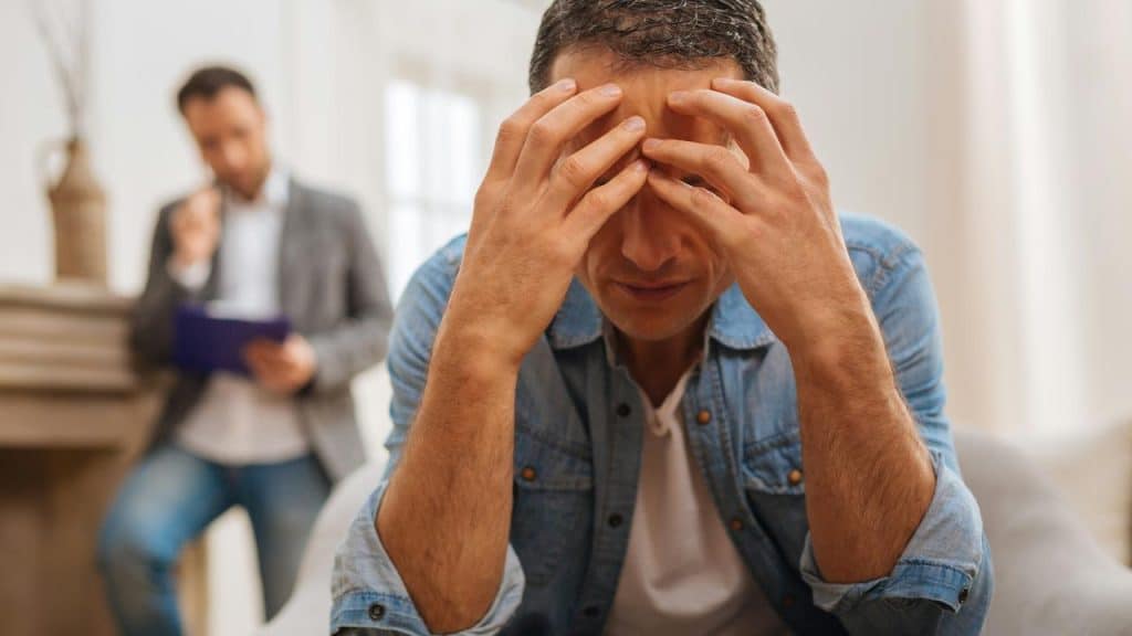 A distressed man sitting on a couch holding his head.