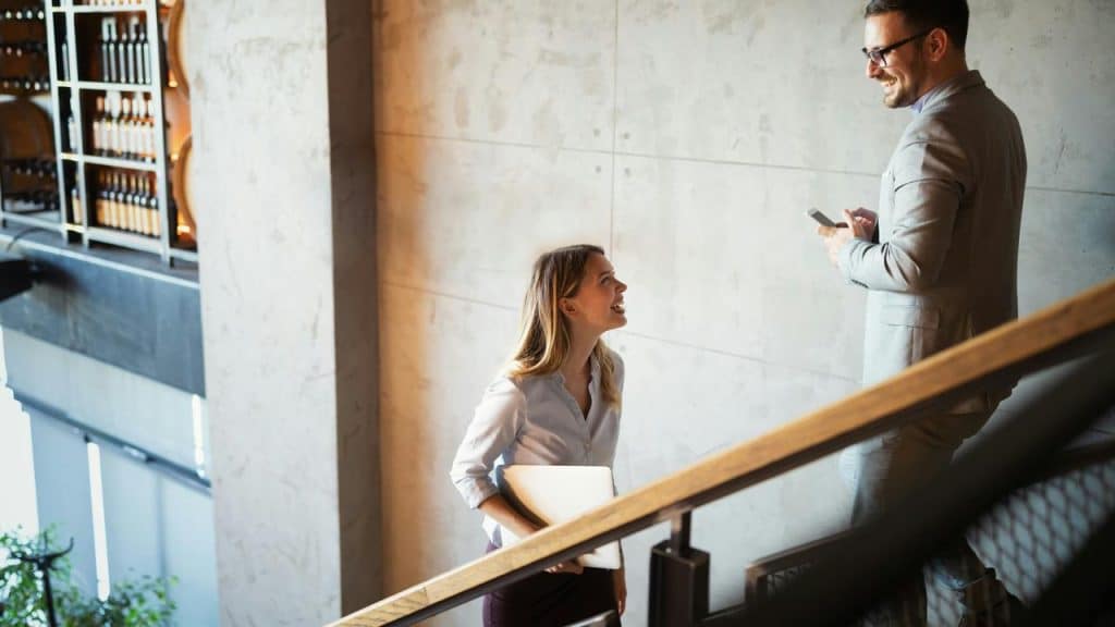 A woman holding a laptop talking to a man on a staircase.