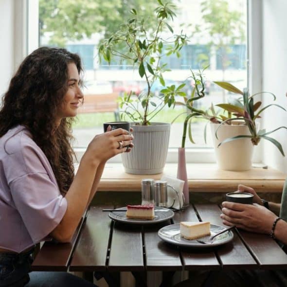 A smiling couple enjoys coffee and cake at a cafe table.