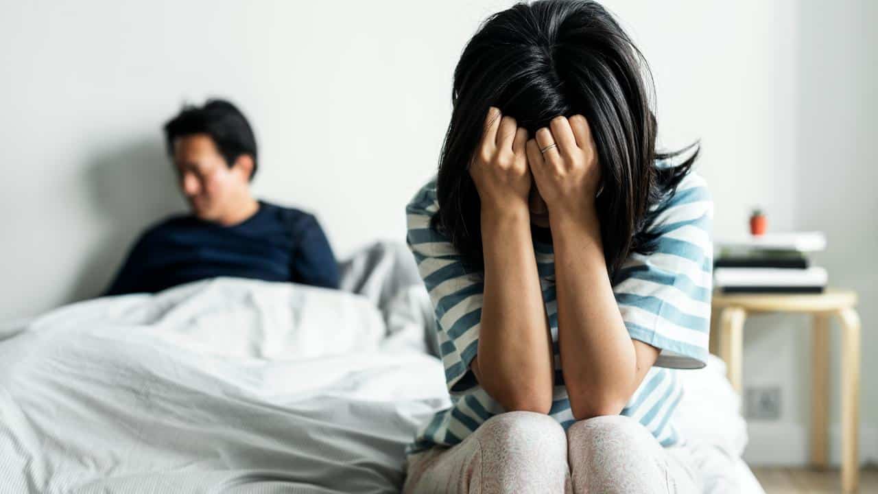 A woman covering her face in bed beside a man.