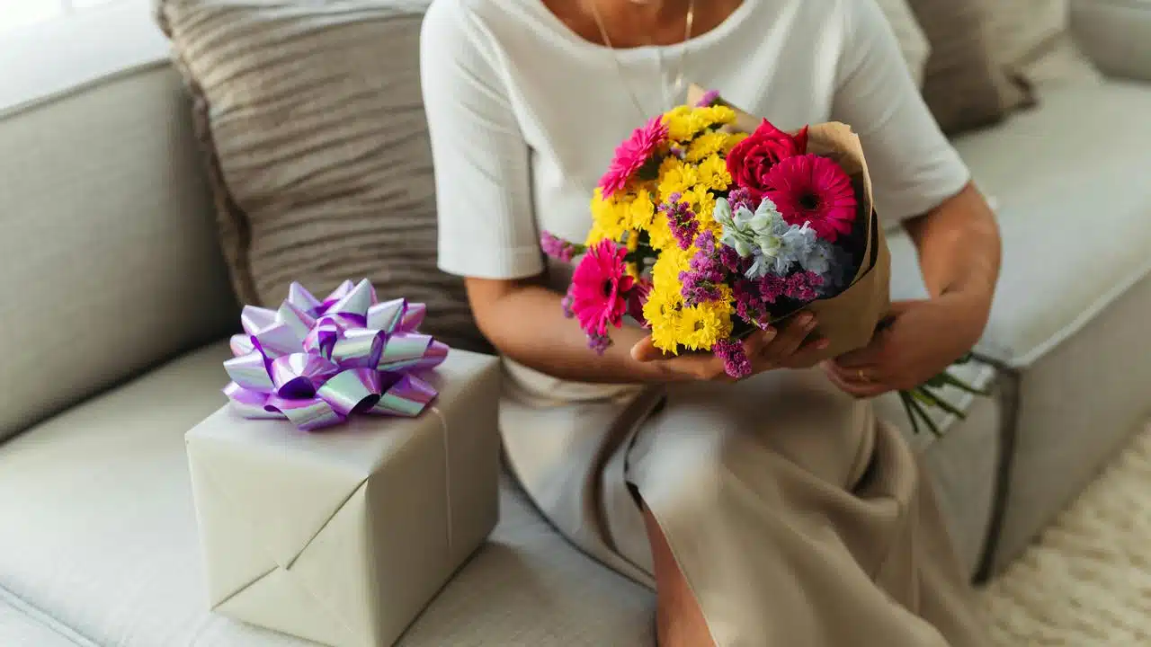 A person holding a colorful bouquet beside a wrapped gift.