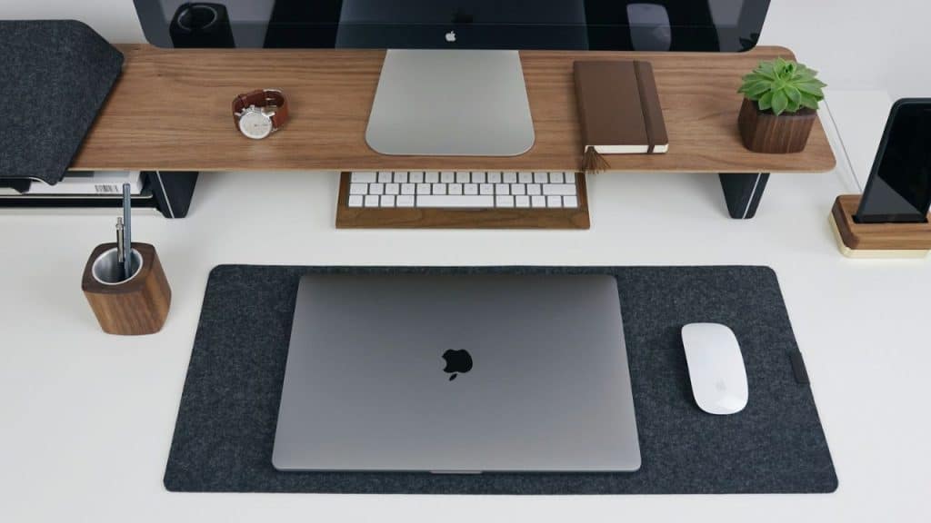 A minimalist desk setup features a laptop, mouse, monitor, and various desk accessories.