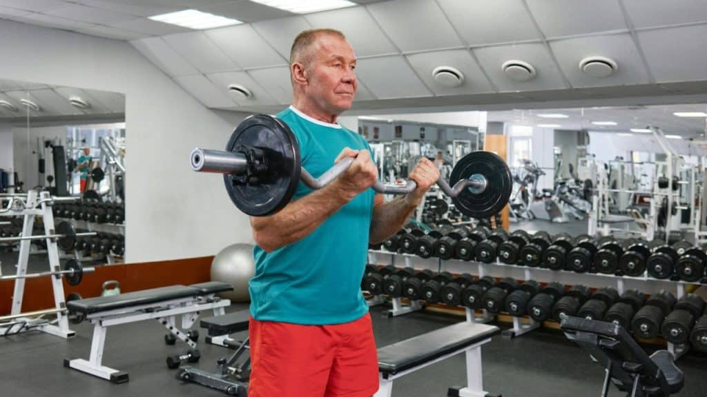 A man in a teal shirt and red shorts lifts weights in a gym.