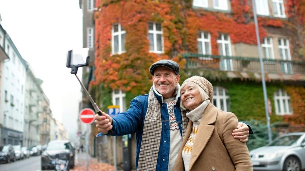 An older couple smiling for a selfie on a city street in autumn.