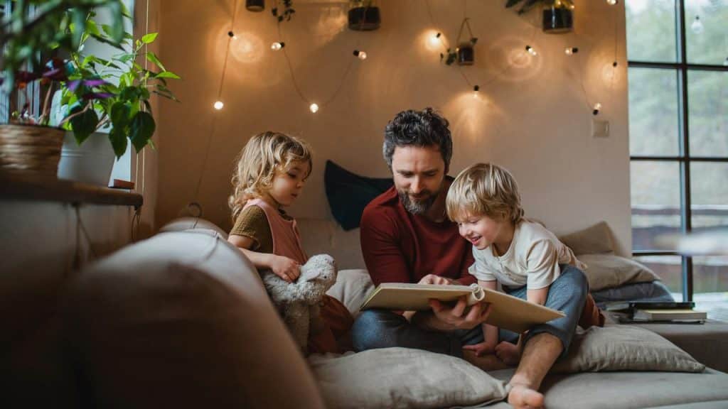 A father reading a book to his two children on a sofa.