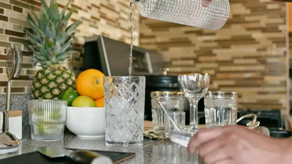 A hand pours water from a textured bottle into a glass.