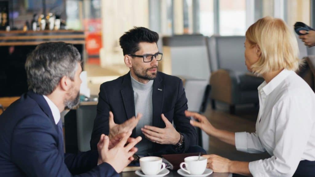 A diverse group of three professionals are having an animated discussion in a cafe.