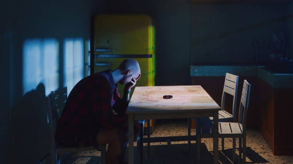 A bald man in a plaid shirt sits alone at a table in a dimly lit kitchen.