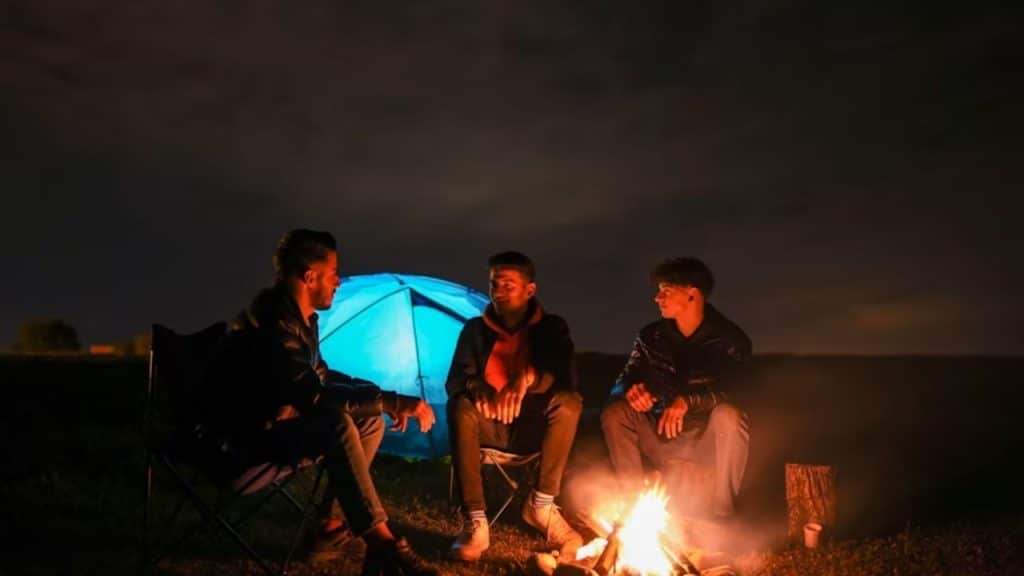 Men gathered around a campfire in a circle for a supportive group conversation outdoors