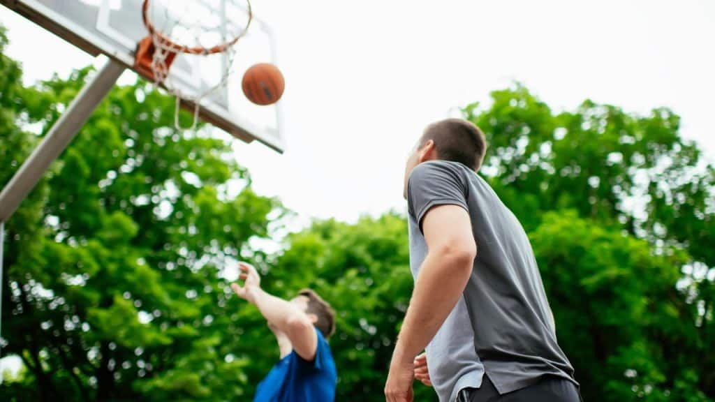A man shooting a basketball toward an outdoor hoop.
