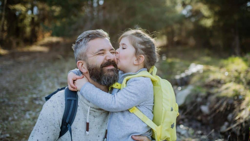 A man receiving a kiss from a child outdoors.
