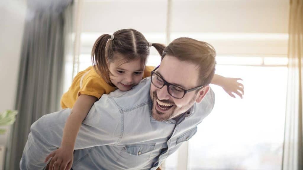 A father wearing glasses giving a piggyback ride to his daughter.
