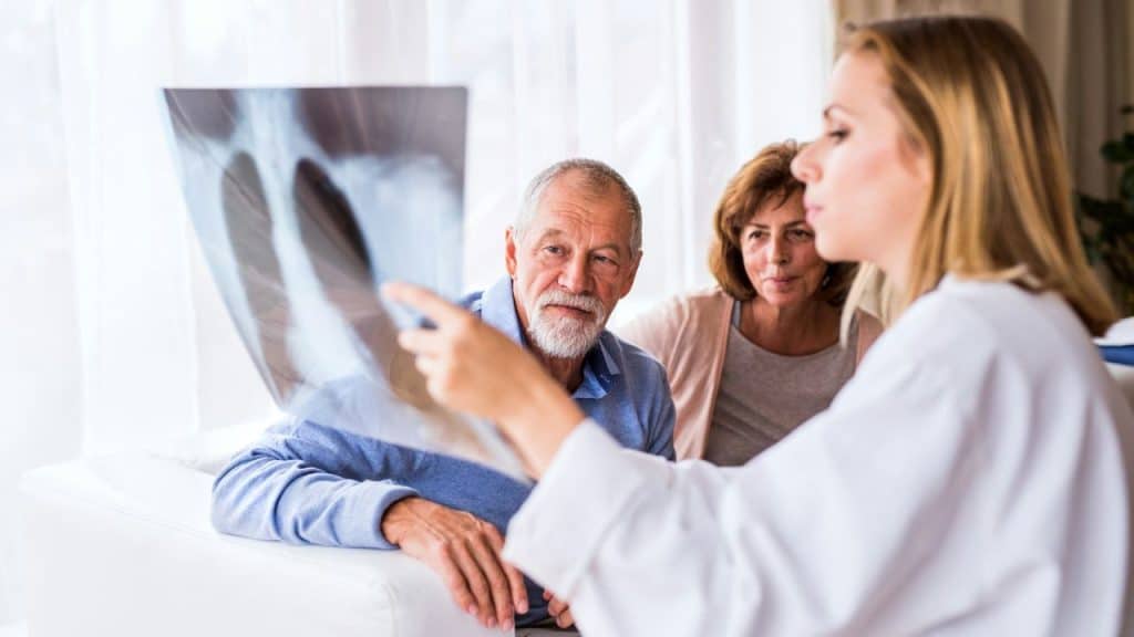 A female doctor points to an X-ray film for two elderly patients.