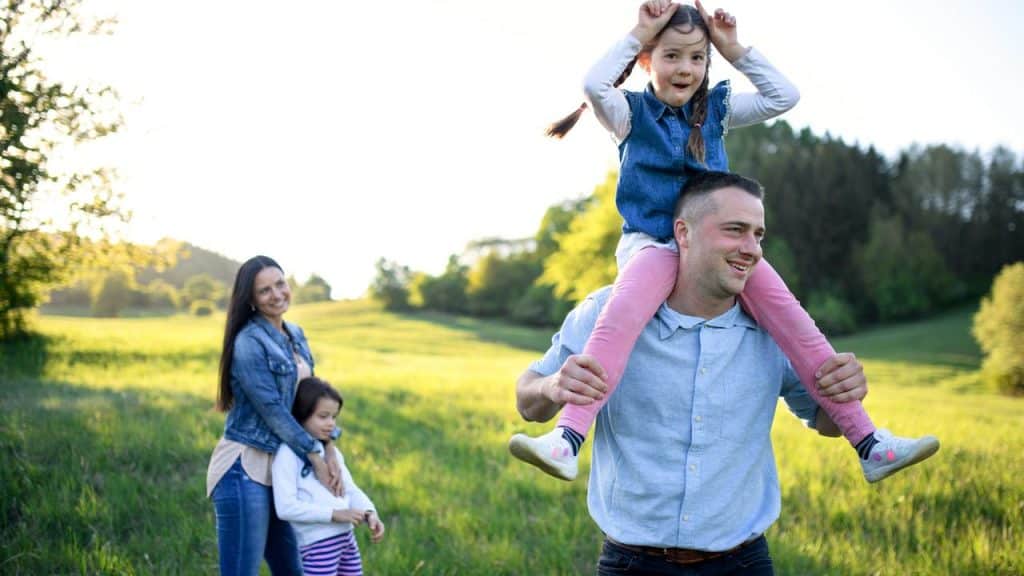 A father carrying a daughter on his shoulders while the mother and younger daughter stand behind.