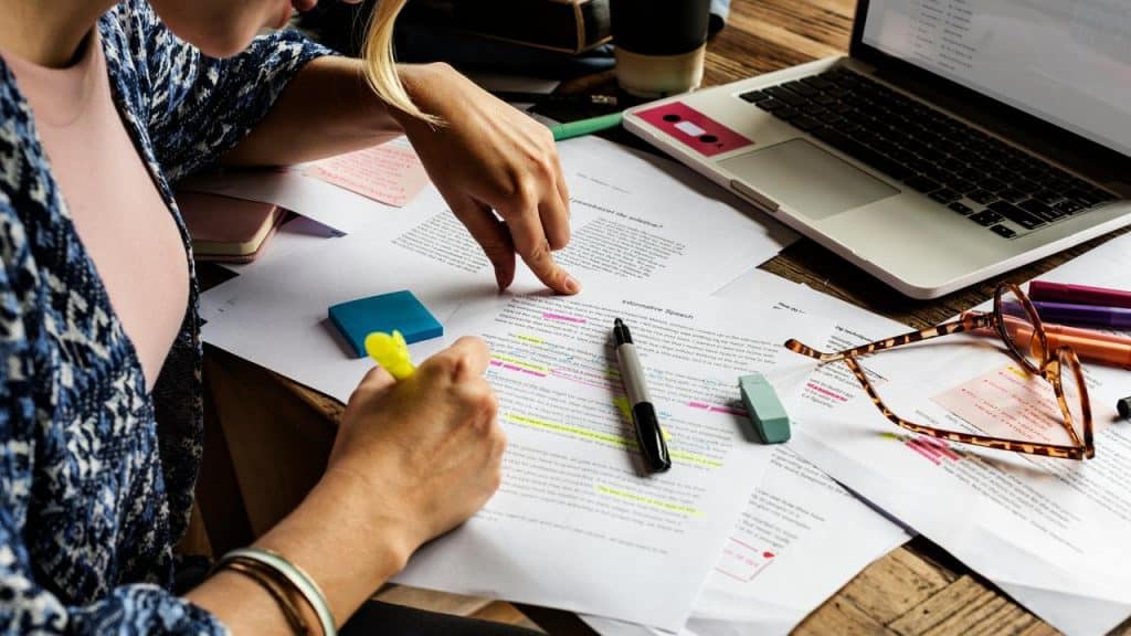 A person highlighting printed documents on a cluttered desk.
