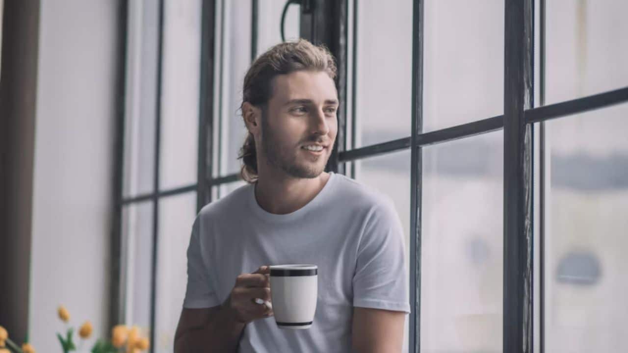 A man enjoying coffee alone smiling while looking out the window.