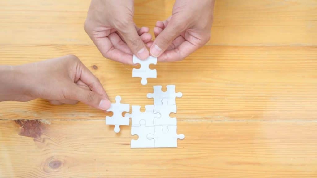Hands of couple assembling a puzzle on the table as a form of relaxation.