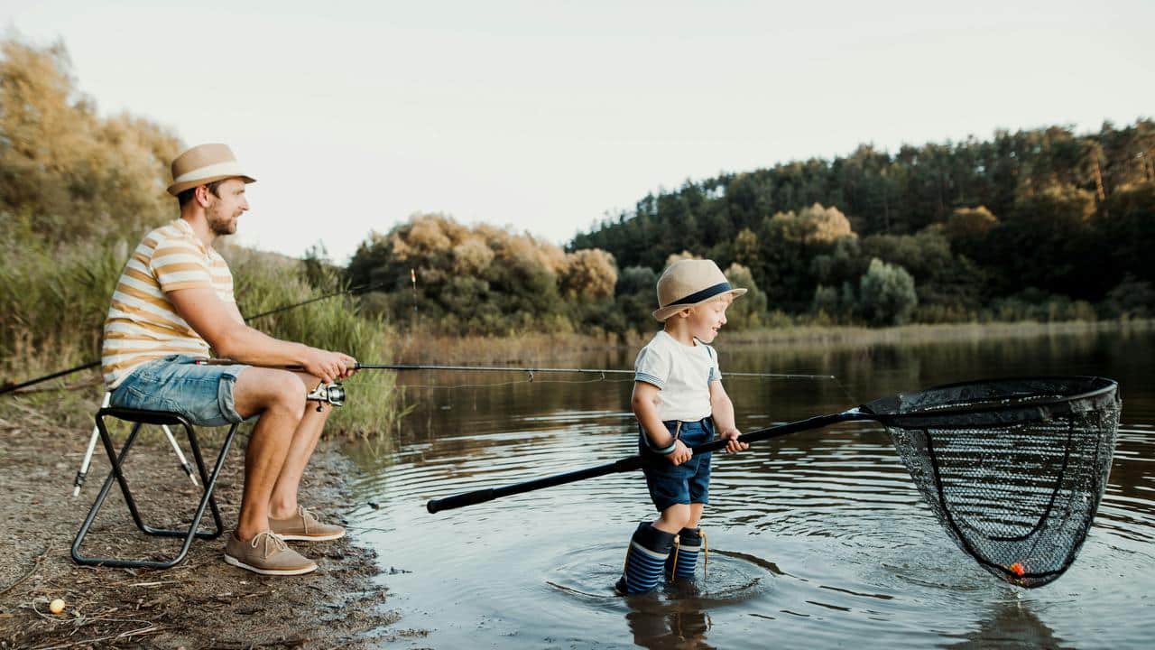A man fishing at a lake with a child holding a net.