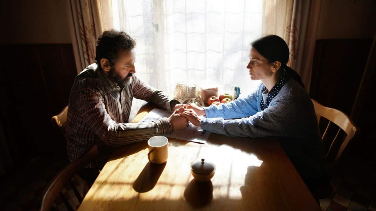 A man and a woman sit across from each other at a table, holding hands.