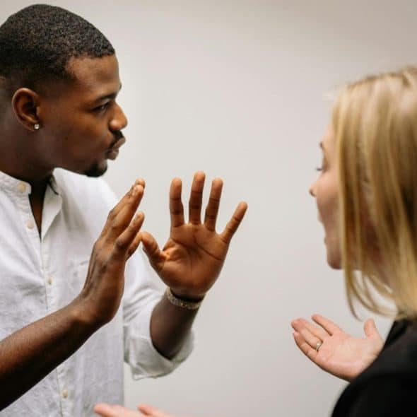 A Black man and a white woman are engaged in a heated argument, gesturing with their hands.