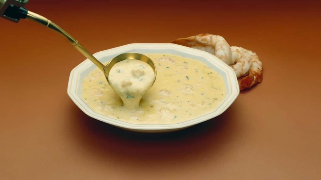 A ladle lifting creamy shrimp chowder from a bowl.