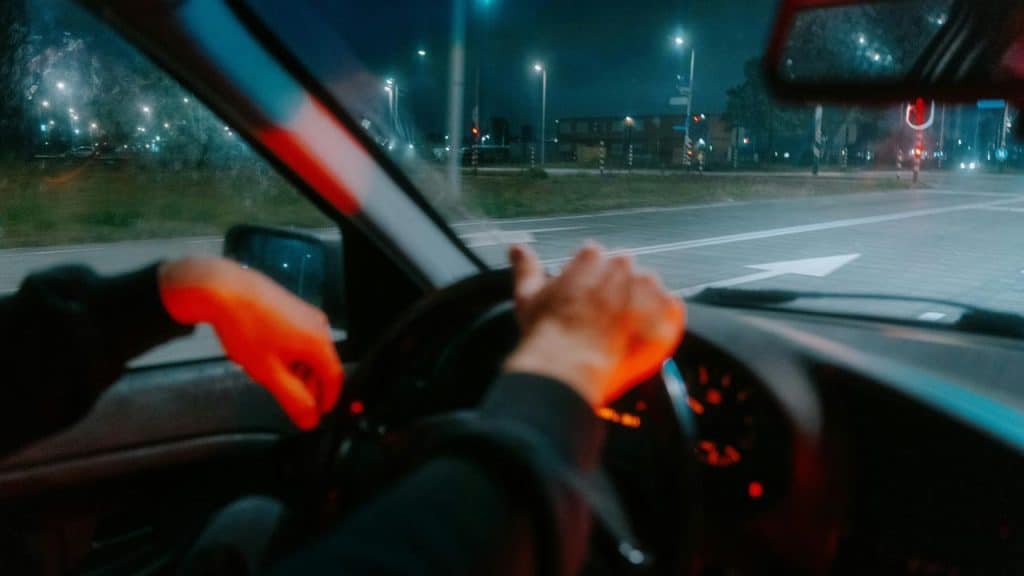 A driver’s hands on a steering wheel at night.