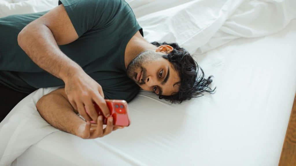 A man lying on a bed holding a smartphone.
