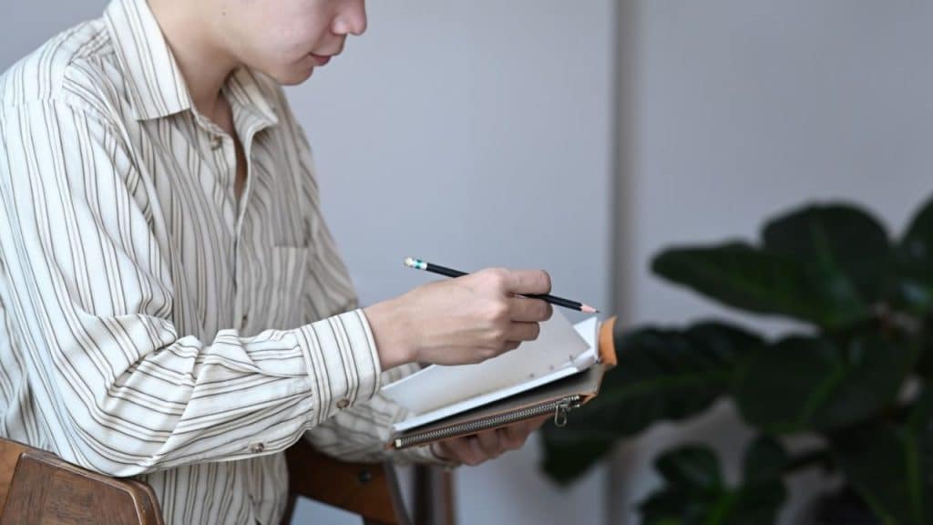 A person in a striped shirt holds a notebook and a pencil.
