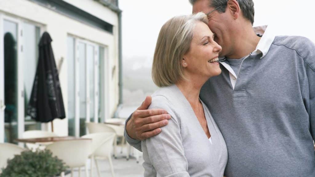 A smiling older couple embracing on a café patio.