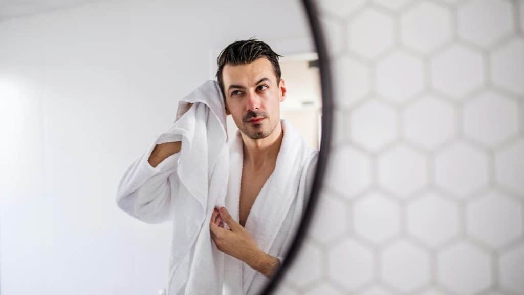 A man in a bathrobe drying his hair with a towel.
