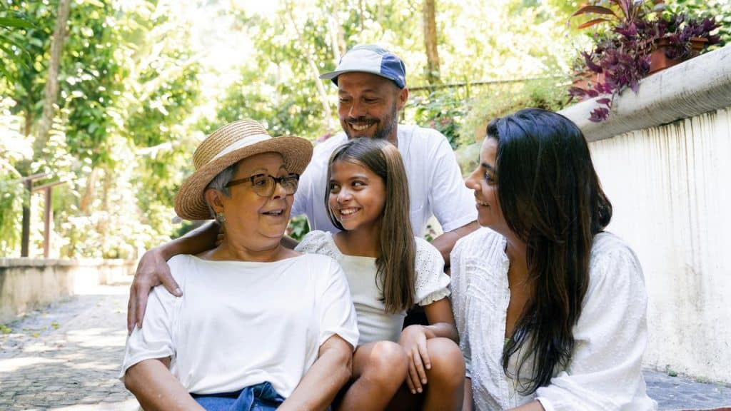 A grandmother, mother, father, and daughter smiling together outdoors.
