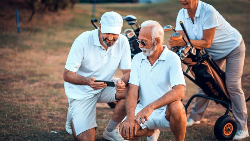 A group of senior golfers checking a phone next to their golf bag.