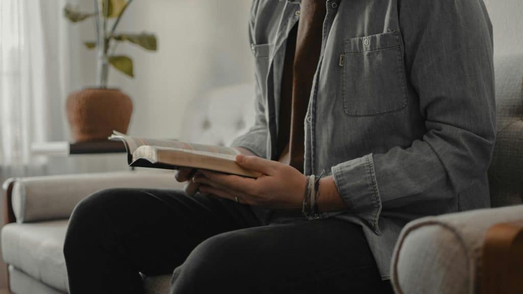 A person seated on a couch reading an open book.