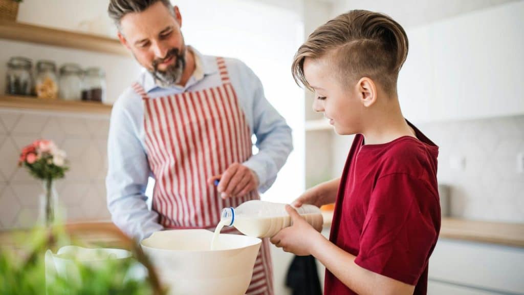 A boy pouring milk into a bowl as his father watches.