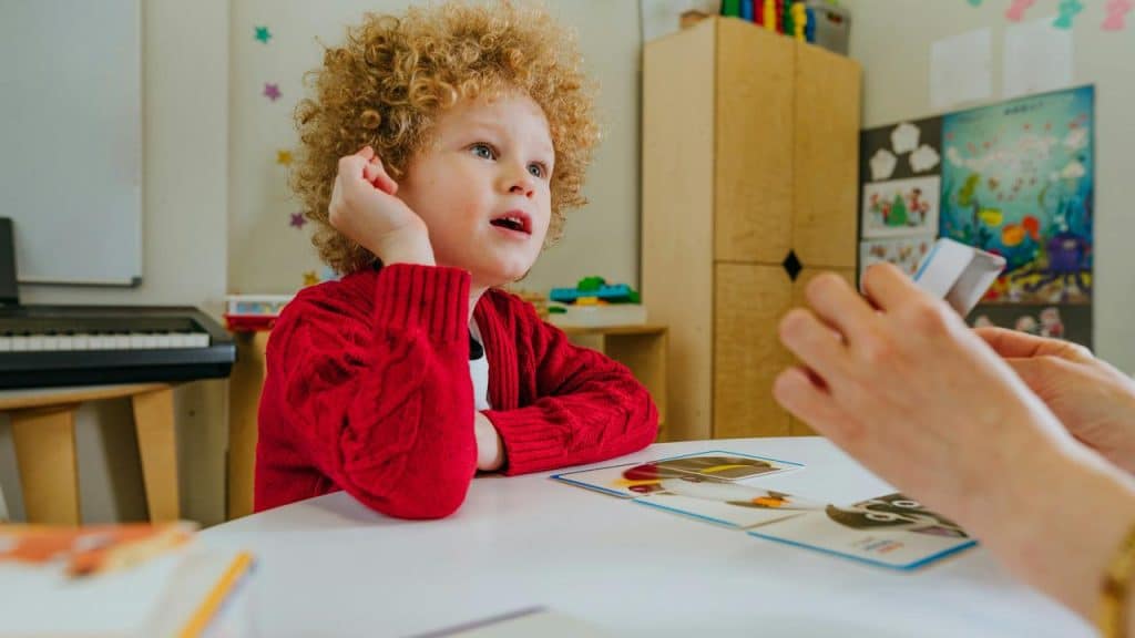 A boy at a table looking at flashcards held by an adult.