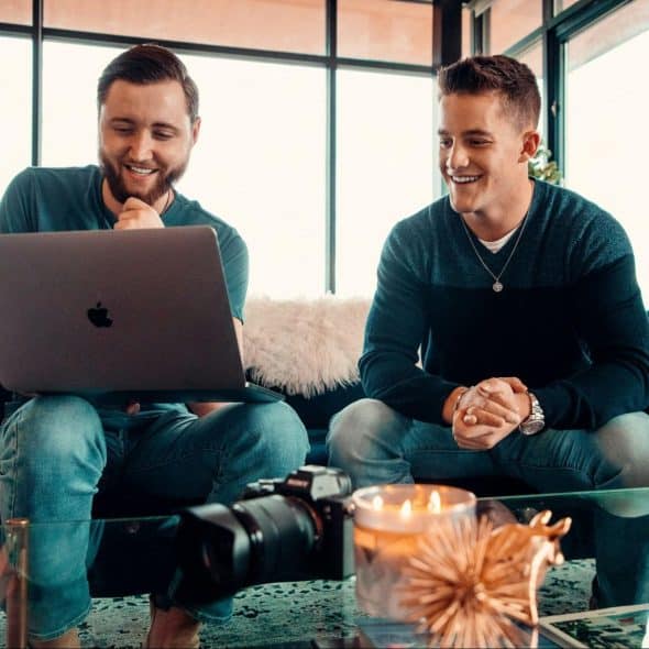 Two men sitting at the couch using a laptop.
