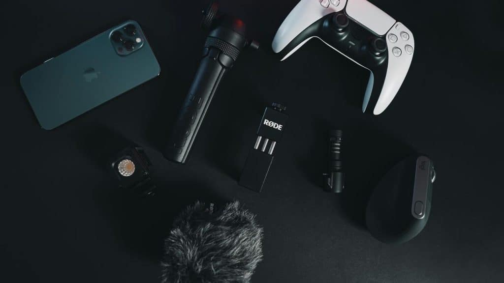 A flat lay of a smartphone, gaming controller, microphones, and a mouse on a dark surface.