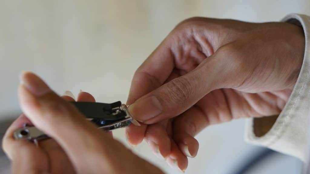 A close-up shot of a person's hands clipping a fingernail with clippers.