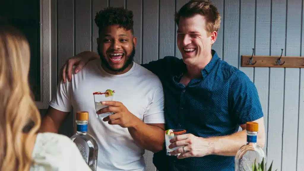 A pair of friends laughing together, each holding a salt-rimmed cocktail.