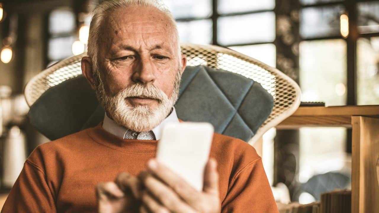 A bearded man in an orange sweater looks at his phone.